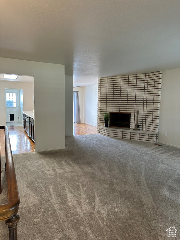 Unfurnished living room featuring a brick fireplace, light colored carpet, and a textured ceiling