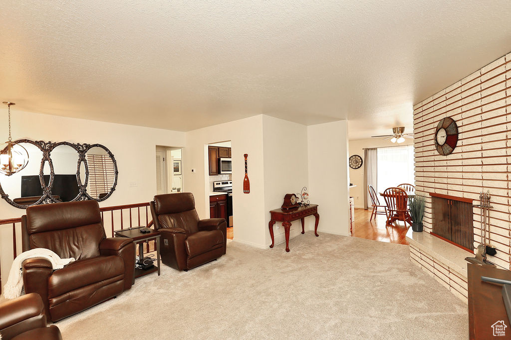 Living room featuring light colored carpet, a brick fireplace, ceiling fan, and a textured ceiling