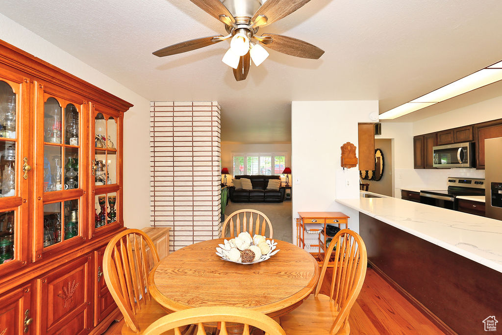 Dining area with brick wall, ceiling fan, and light hardwood / wood-style flooring