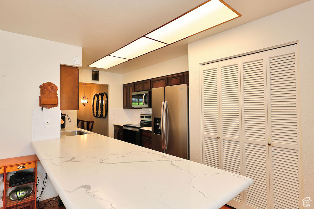 Kitchen with stainless steel appliances, sink, light stone counters, and kitchen peninsula