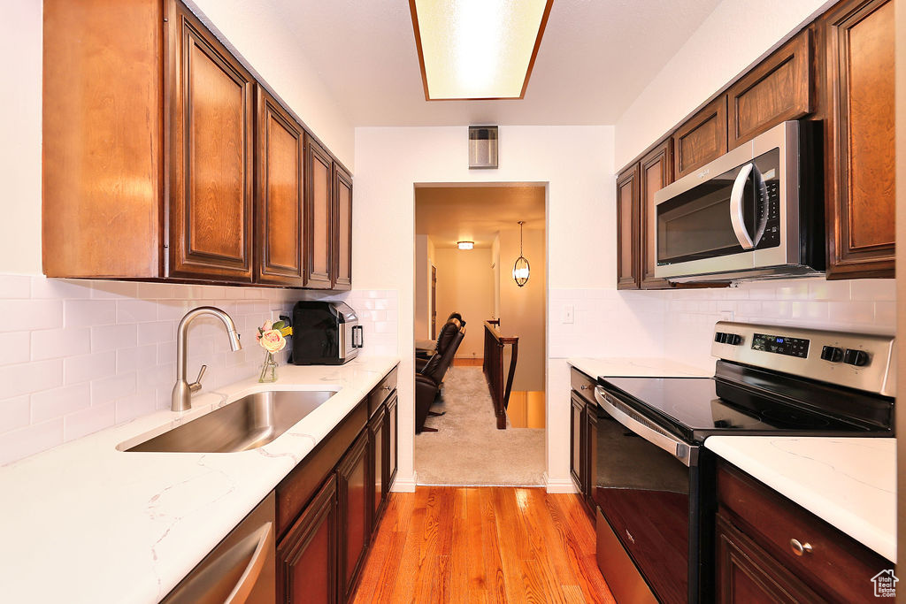 Kitchen with light stone countertops, sink, light hardwood / wood-style flooring, and appliances with stainless steel finishes