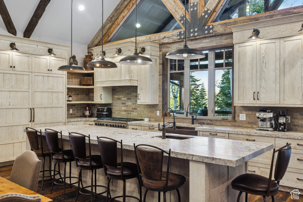 Kitchen with hanging light fixtures, beamed ceiling, a center island with sink, and plenty of natural light