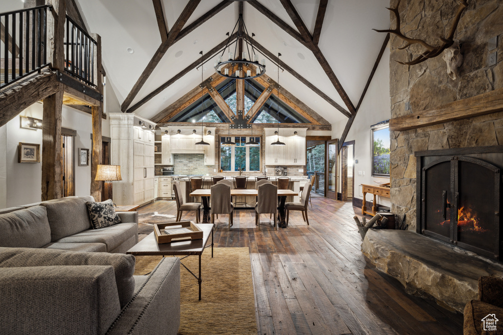 Living room with high vaulted ceiling, beamed ceiling, a stone fireplace, and wood-type flooring