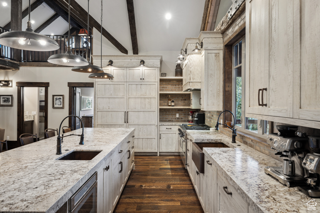 Kitchen with decorative light fixtures, a center island with sink, sink, and beam ceiling