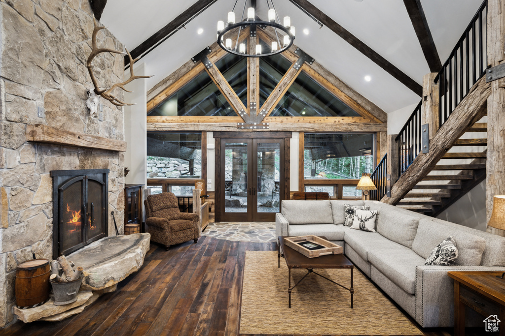 Living room featuring a stone fireplace, beamed ceiling, wood-type flooring, an inviting chandelier, and high vaulted ceiling