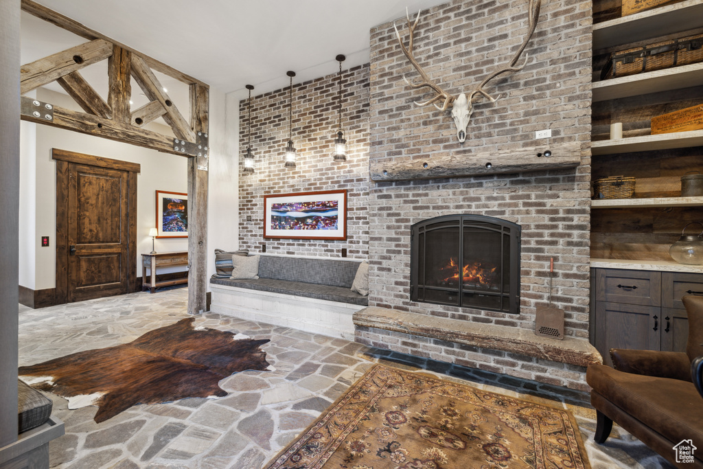 Living room with brick wall, beamed ceiling, built in shelves, a brick fireplace, and high vaulted ceiling