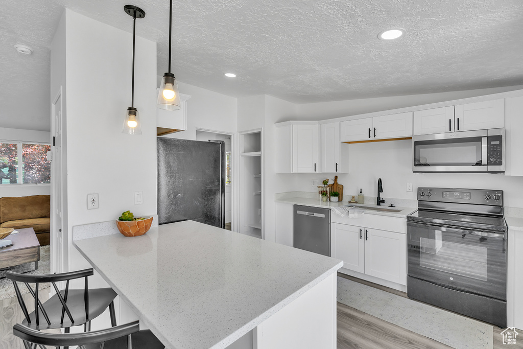 Kitchen with white cabinetry, light wood-type flooring, black appliances, pendant lighting, and sink