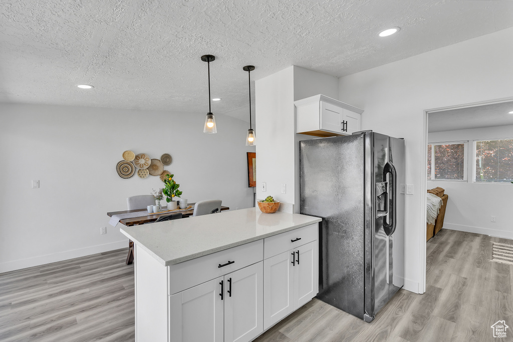 Kitchen featuring black fridge, white cabinets, light hardwood / wood-style floors, and kitchen peninsula