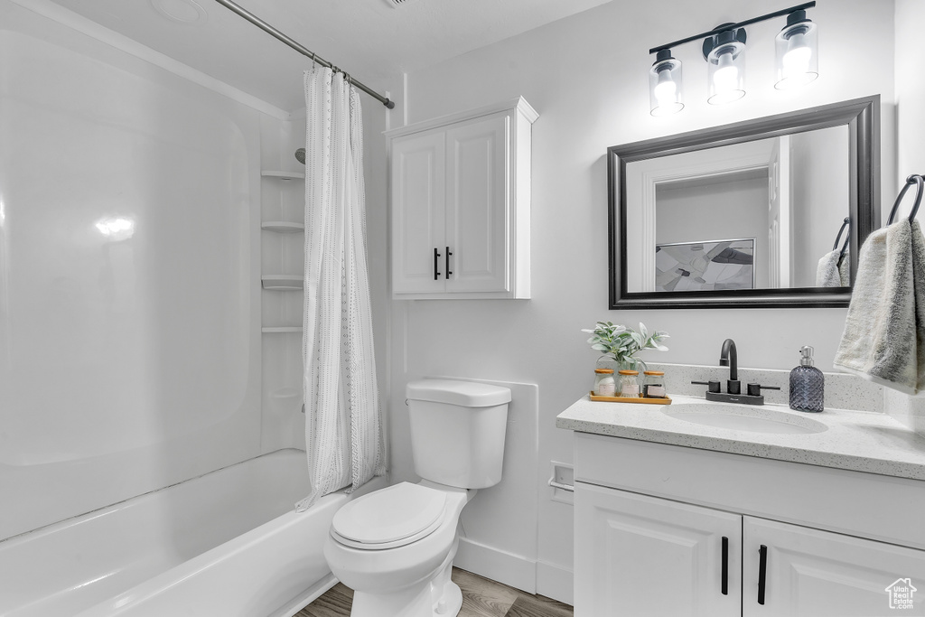 Full bathroom featuring wood-type flooring, shower / bath combination with curtain, vanity, and toilet