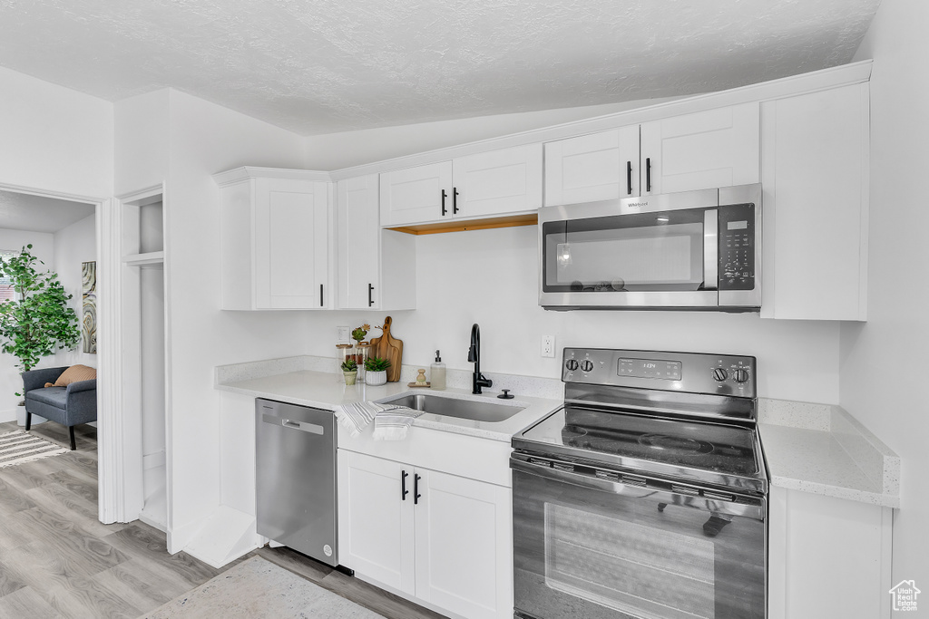 Kitchen with stainless steel appliances, white cabinetry, light wood-type flooring, sink, and lofted ceiling