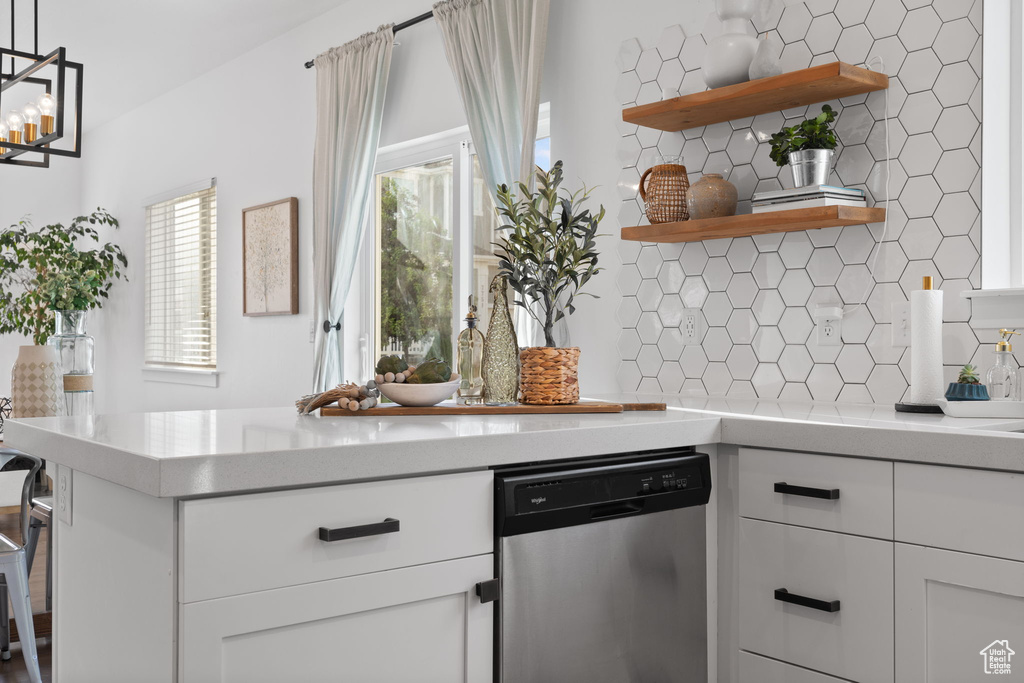 Kitchen featuring decorative light fixtures, an inviting chandelier, tasteful backsplash, stainless steel dishwasher, and white cabinets