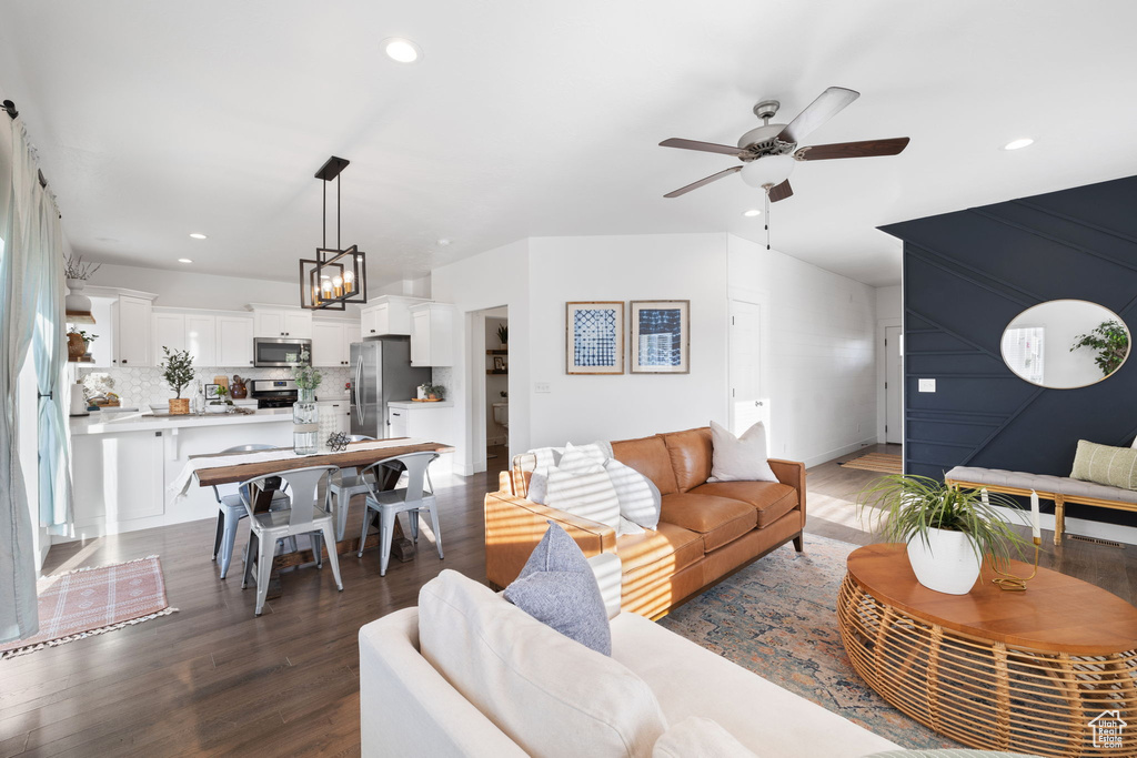 Living room featuring ceiling fan with notable chandelier and dark wood-type flooring