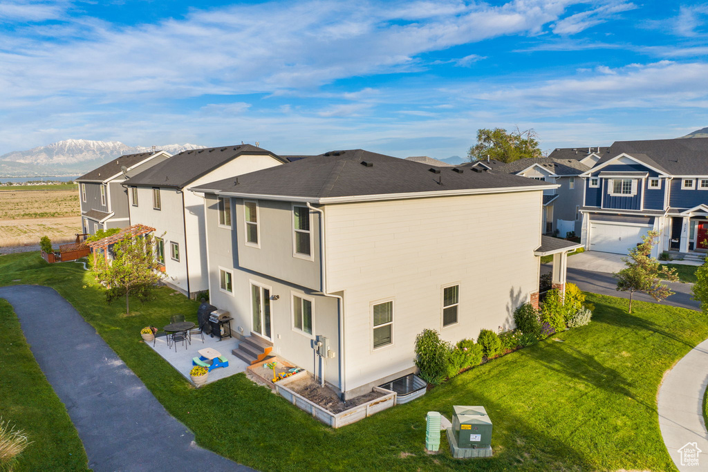 Rear view of house with a garage, a mountain view, a lawn, and a patio area