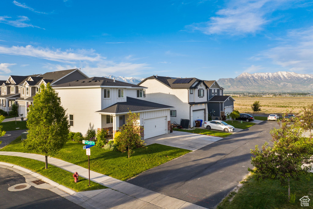 View of front of house with a front yard, a garage, a mountain view, and solar panels