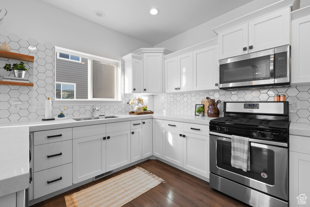 Kitchen with stainless steel appliances, dark wood-type flooring, backsplash, sink, and white cabinetry