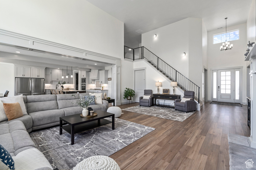 Living room with a high ceiling, a notable chandelier, a wealth of natural light, and dark wood-type flooring