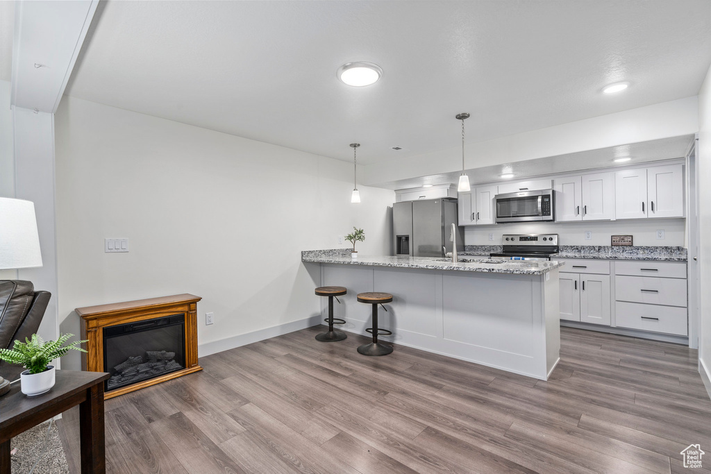 Kitchen with appliances with stainless steel finishes, white cabinets, wood-type flooring, and light stone counters