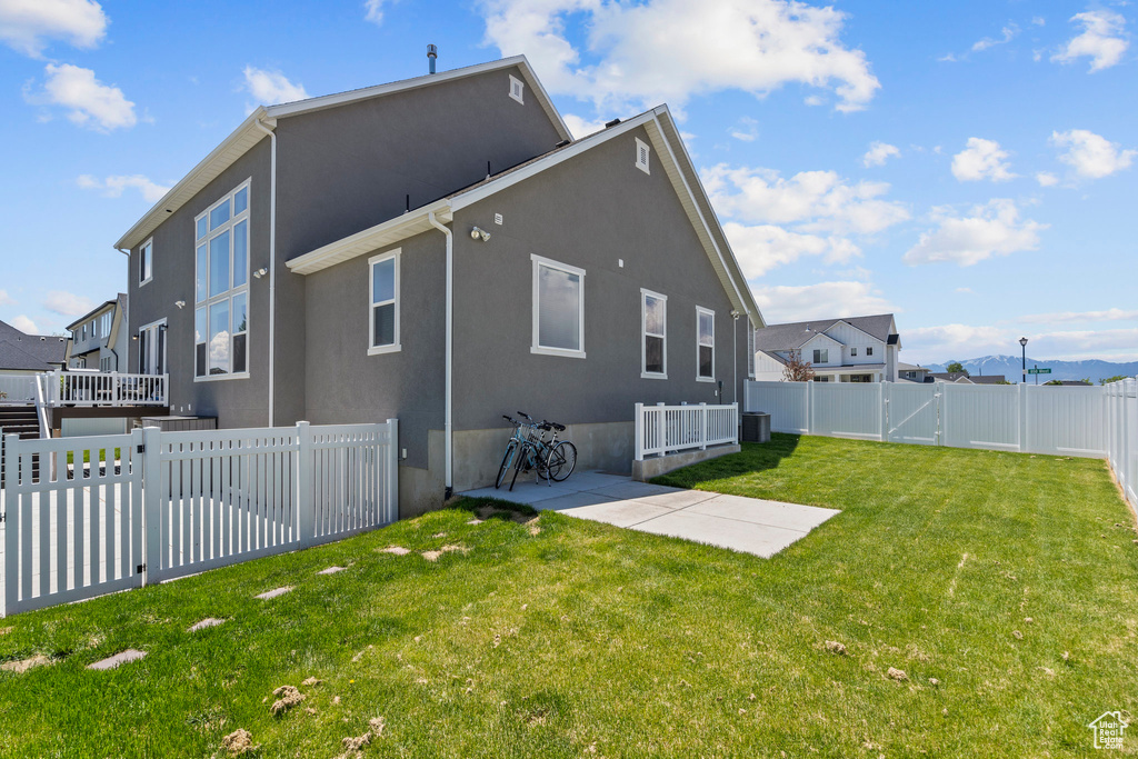 Back of property with central AC, a lawn, and a patio