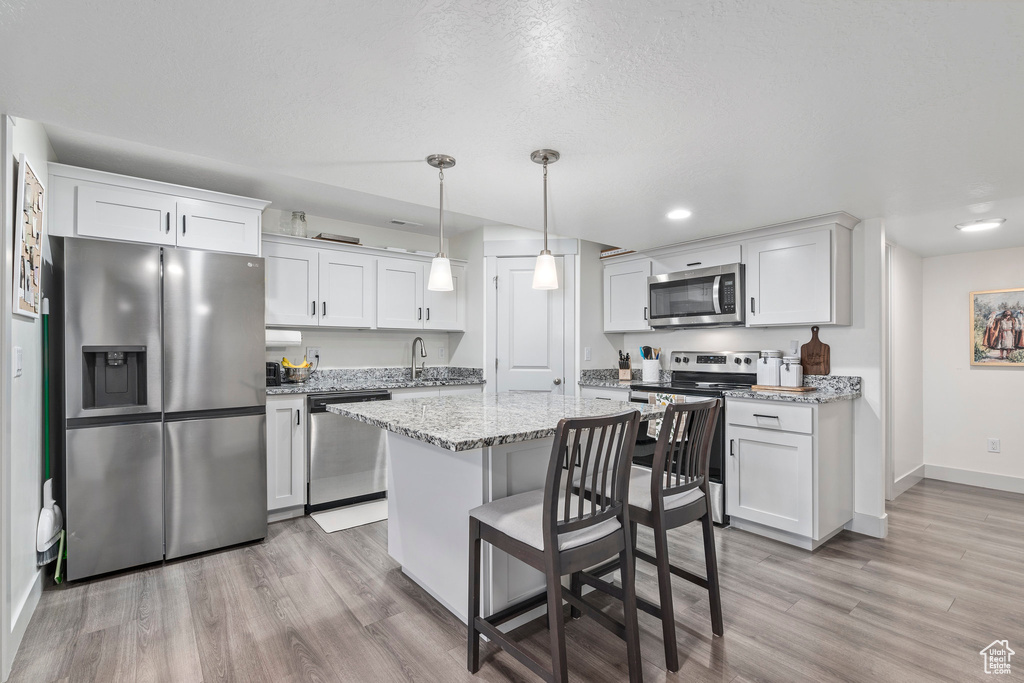 Kitchen featuring decorative light fixtures, light wood-type flooring, a kitchen island, white cabinetry, and appliances with stainless steel finishes