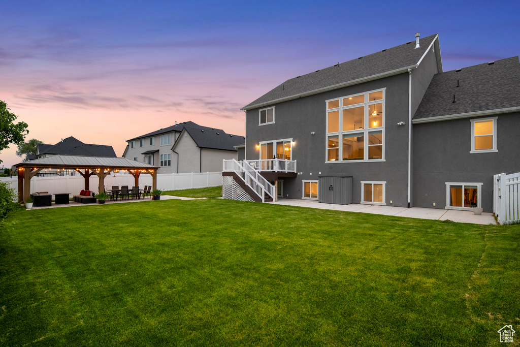 Back house at dusk featuring a lawn, a gazebo, and a patio