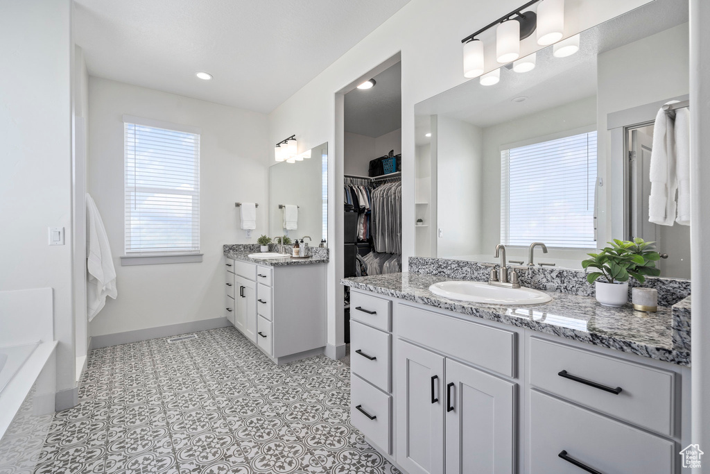 Bathroom with tile flooring, vanity with extensive cabinet space, a bath to relax in, and a wealth of natural light