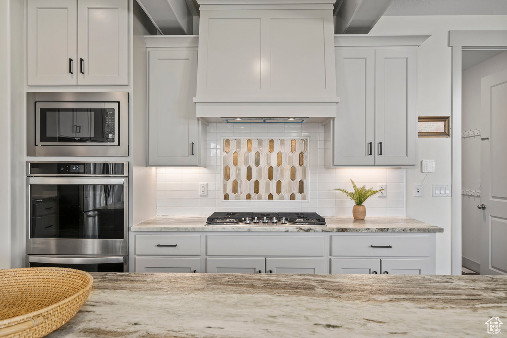 Kitchen with appliances with stainless steel finishes, white cabinets, light stone countertops, and tasteful backsplash