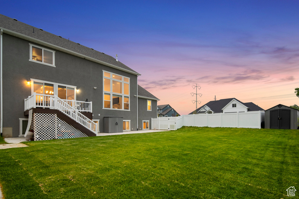 Back house at dusk with a patio, a storage unit, and a lawn