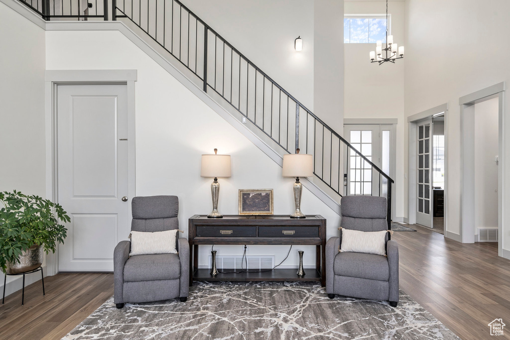 Living area with a high ceiling, wood-type flooring, and an inviting chandelier