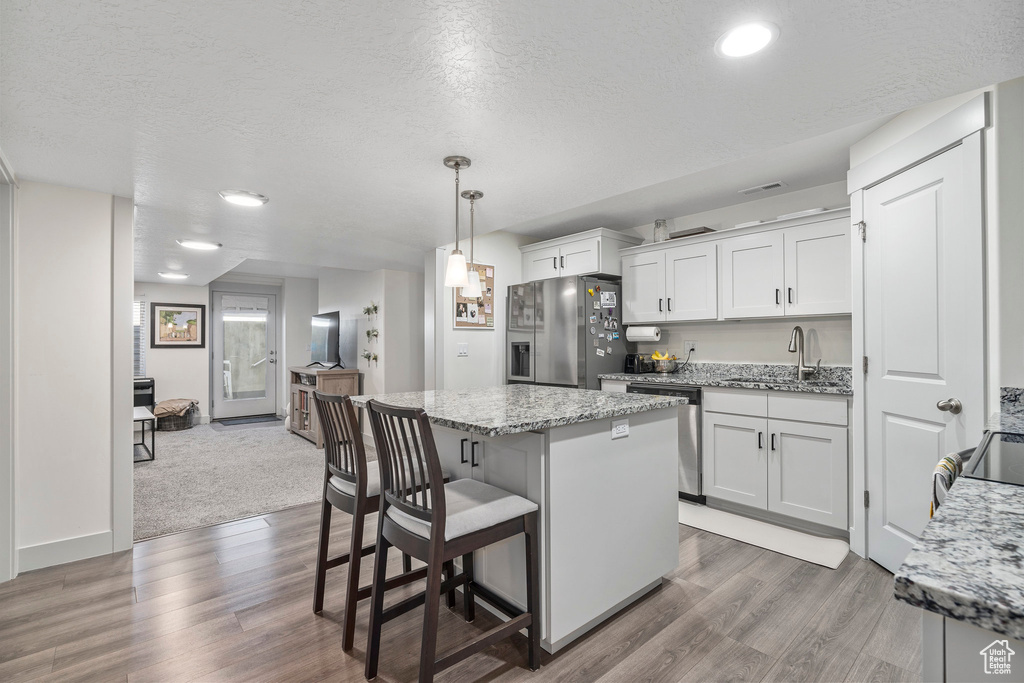 Kitchen featuring decorative light fixtures, wood-type flooring, sink, white cabinetry, and appliances with stainless steel finishes