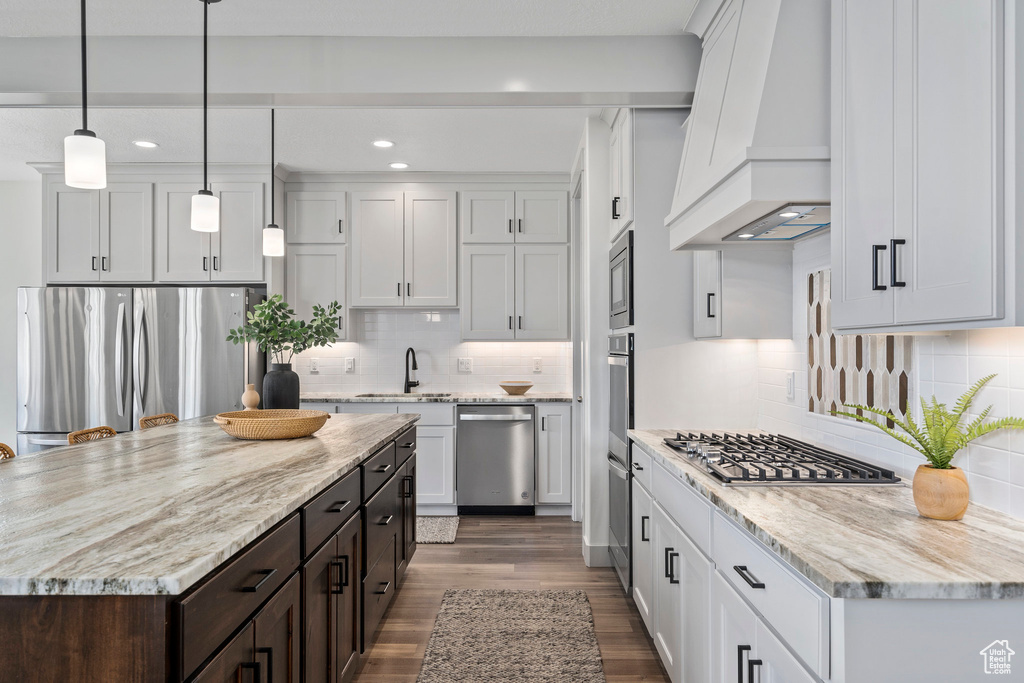 Kitchen with custom range hood, stainless steel appliances, backsplash, and wood-type flooring