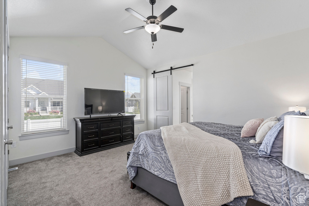 Carpeted bedroom with a barn door, ceiling fan, and vaulted ceiling