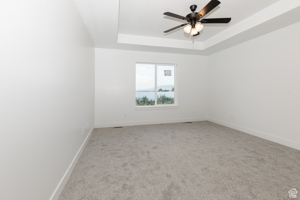 Carpeted spare room with ceiling fan and a tray ceiling