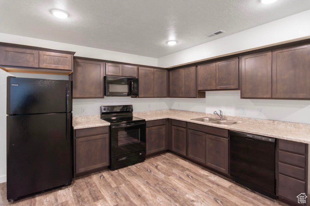 Kitchen with black appliances, sink, light hardwood / wood-style floors, and dark brown cabinets