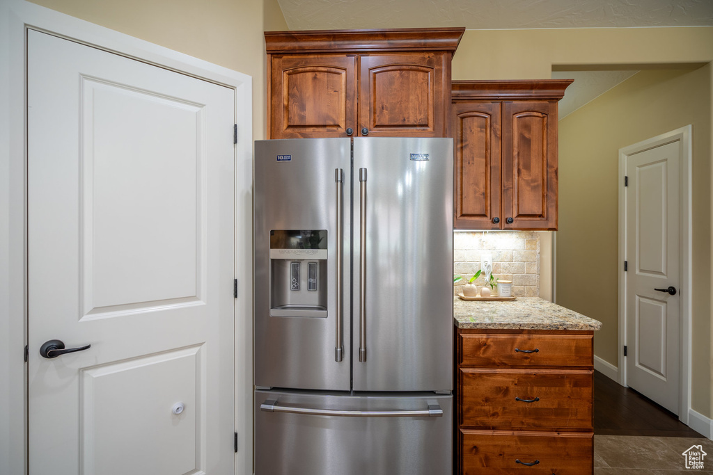 Kitchen featuring stainless steel fridge with ice dispenser, backsplash, dark wood-type flooring, and light stone counters