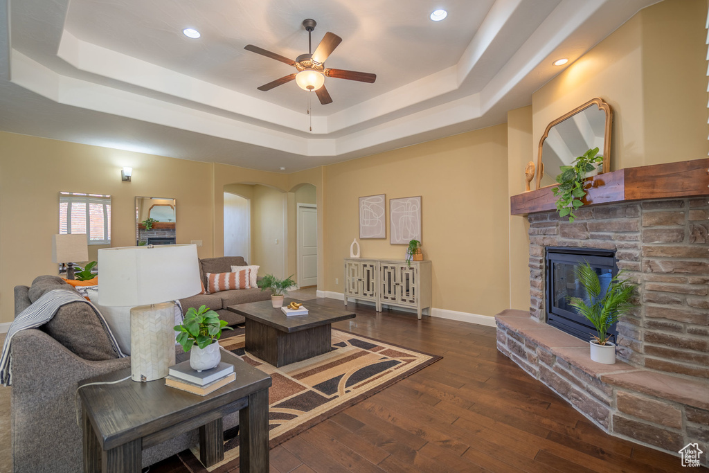 Living room with ceiling fan, a tray ceiling, a fireplace, and dark hardwood / wood-style flooring