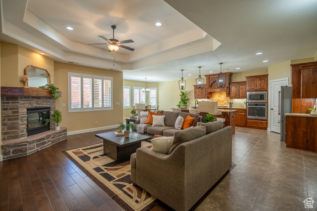 Living room featuring dark hardwood / wood-style flooring, a tray ceiling, a stone fireplace, sink, and ceiling fan