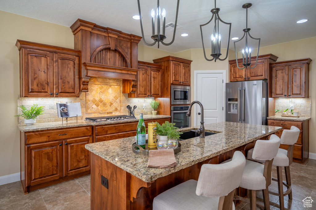 Kitchen with stainless steel appliances, light tile floors, backsplash, and a kitchen island with sink