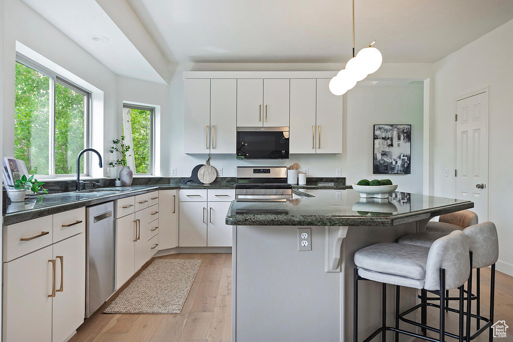 Kitchen with light hardwood / wood-style flooring, decorative light fixtures, a kitchen island, sink, and appliances with stainless steel finishes