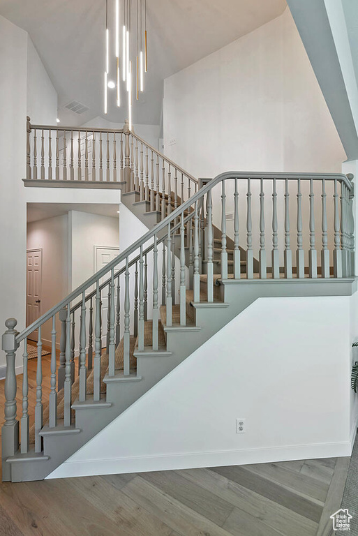 Staircase featuring high vaulted ceiling, hardwood / wood-style floors, and a notable chandelier