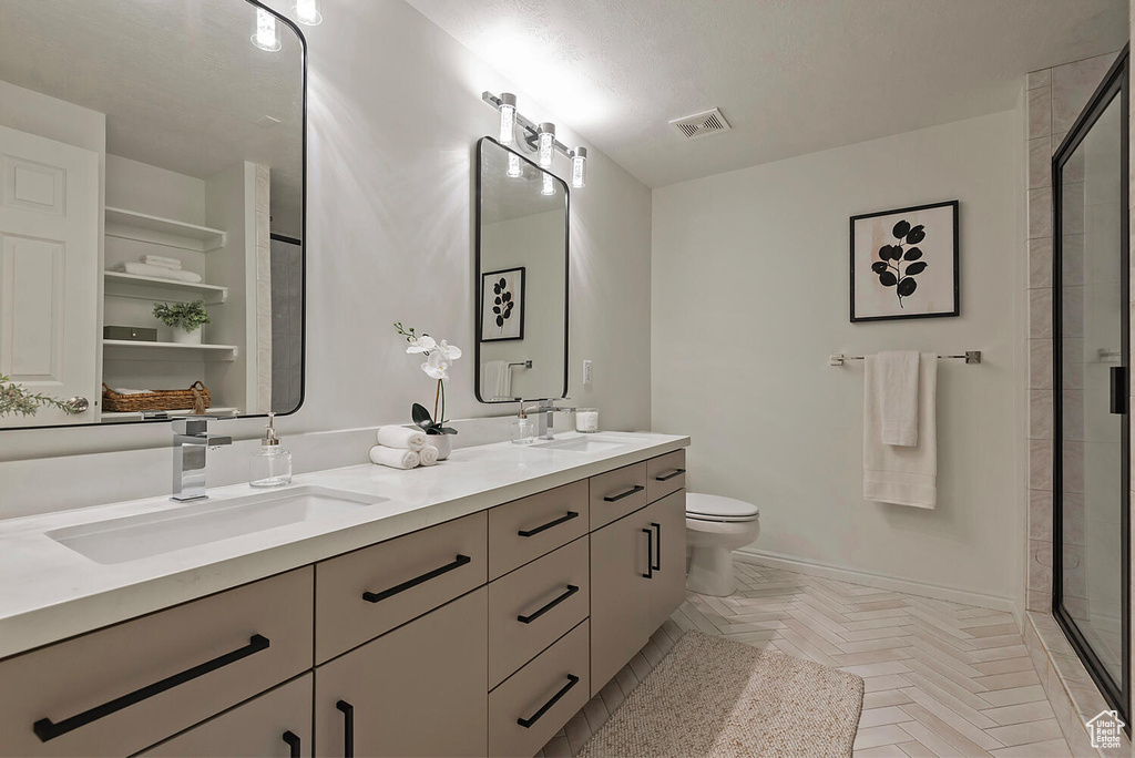 Bathroom with an enclosed shower, dual bowl vanity, parquet flooring, and toilet