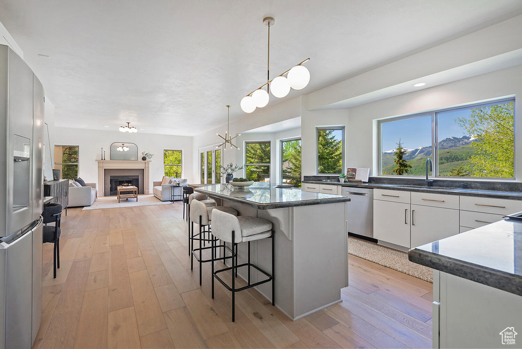 Kitchen with light hardwood / wood-style flooring, hanging light fixtures, a center island, white cabinets, and appliances with stainless steel finishes