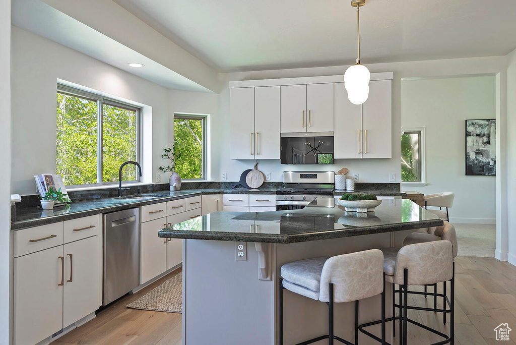 Kitchen featuring a center island, light wood-type flooring, stainless steel appliances, decorative light fixtures, and a breakfast bar