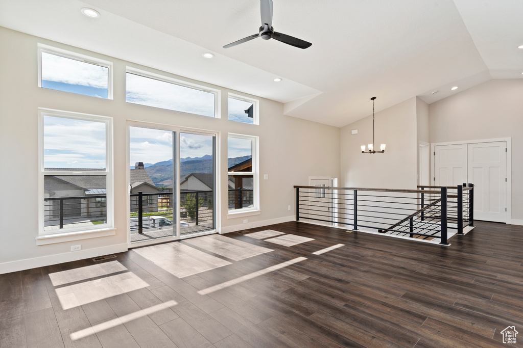 Empty room featuring ceiling fan with notable chandelier, dark wood-type flooring, and high vaulted ceiling