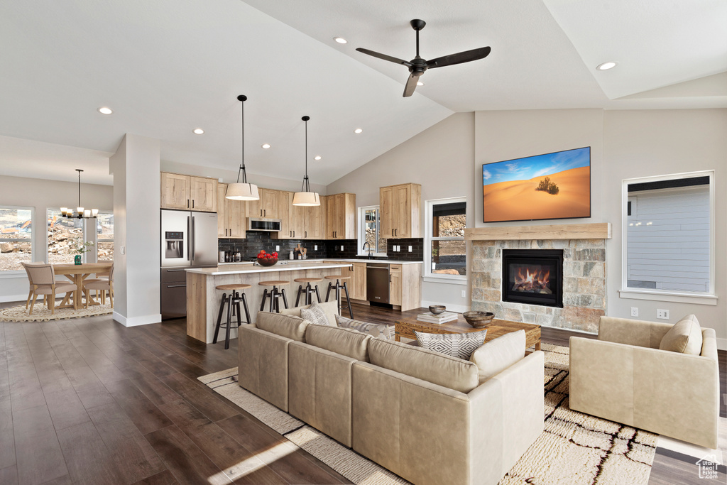 Living room with a stone fireplace, ceiling fan with notable chandelier, plenty of natural light, and dark hardwood / wood-style flooring