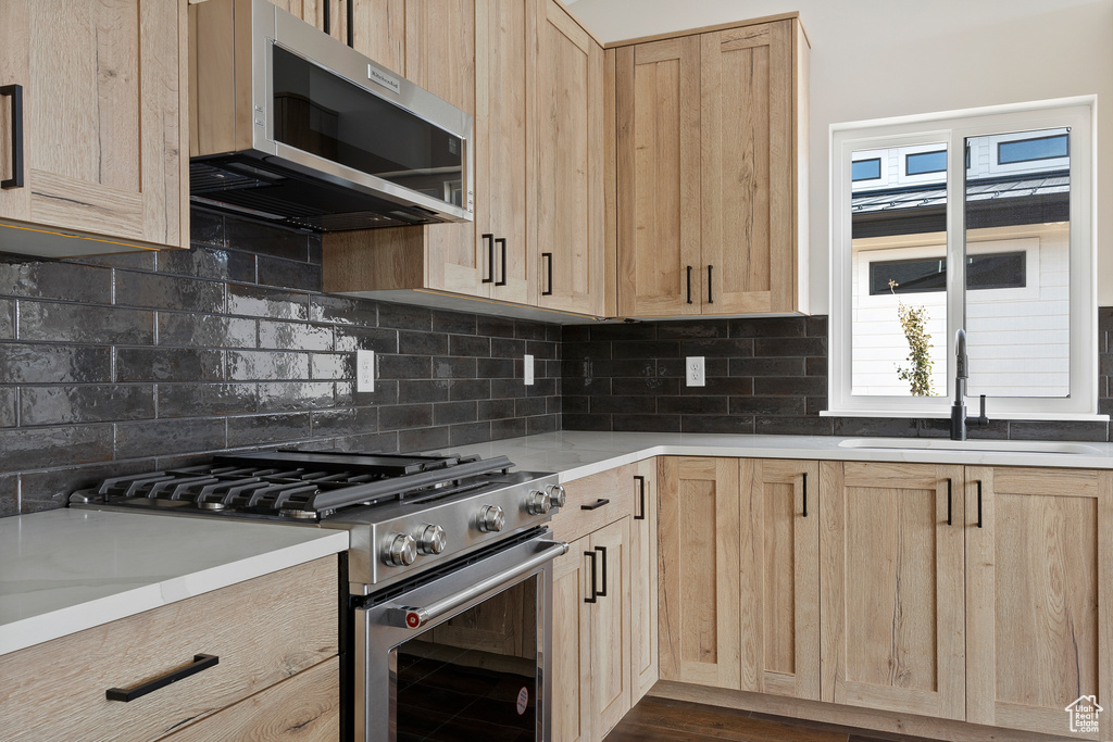 Kitchen featuring appliances with stainless steel finishes, backsplash, light brown cabinets, dark hardwood / wood-style flooring, and sink