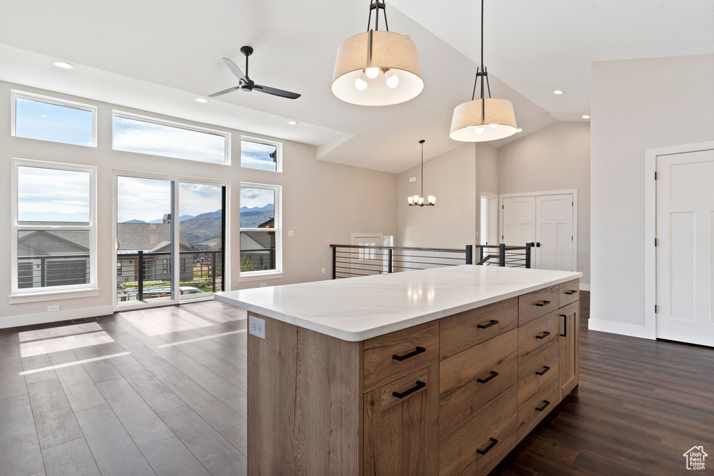 Kitchen featuring ceiling fan with notable chandelier, a center island, dark wood-type flooring, and pendant lighting