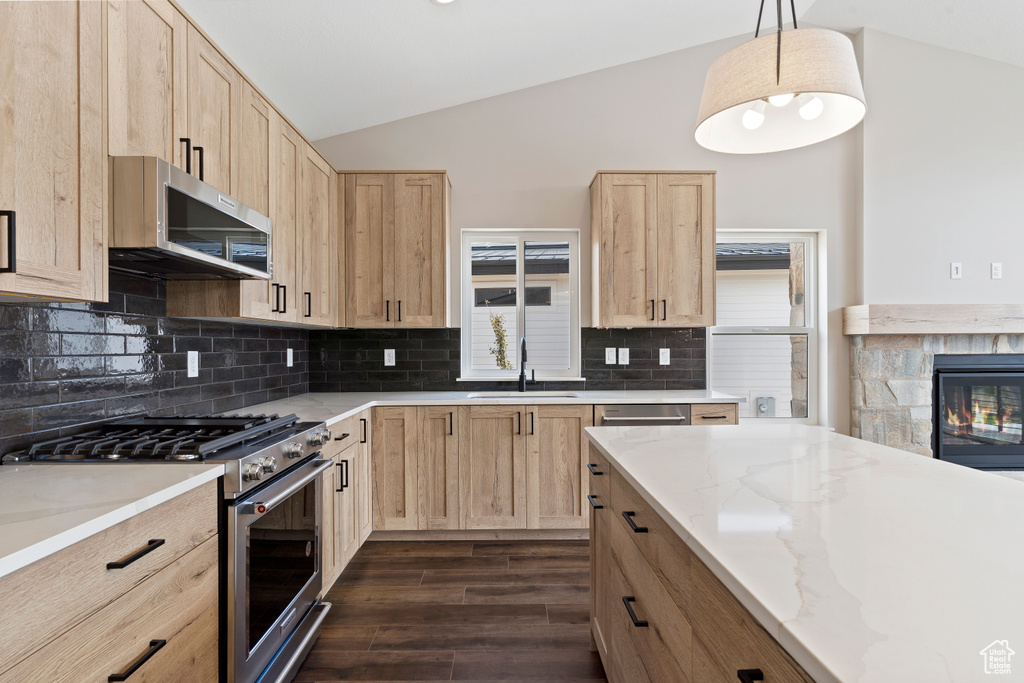 Kitchen with light brown cabinetry, vaulted ceiling, appliances with stainless steel finishes, and sink