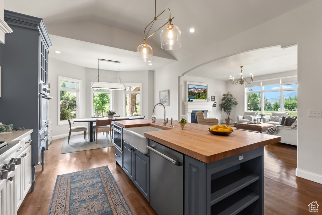 Kitchen with a center island with sink, decorative light fixtures, dark wood-type flooring, wood counters, and appliances with stainless steel finishes