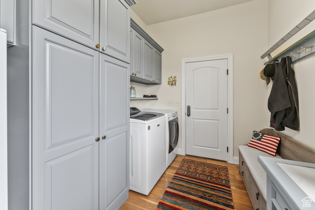 Clothes washing area featuring separate washer and dryer, light wood-type flooring, and cabinets