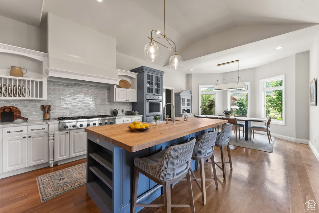 Kitchen featuring tasteful backsplash, butcher block counters, a kitchen island with sink, hardwood / wood-style floors, and appliances with stainless steel finishes